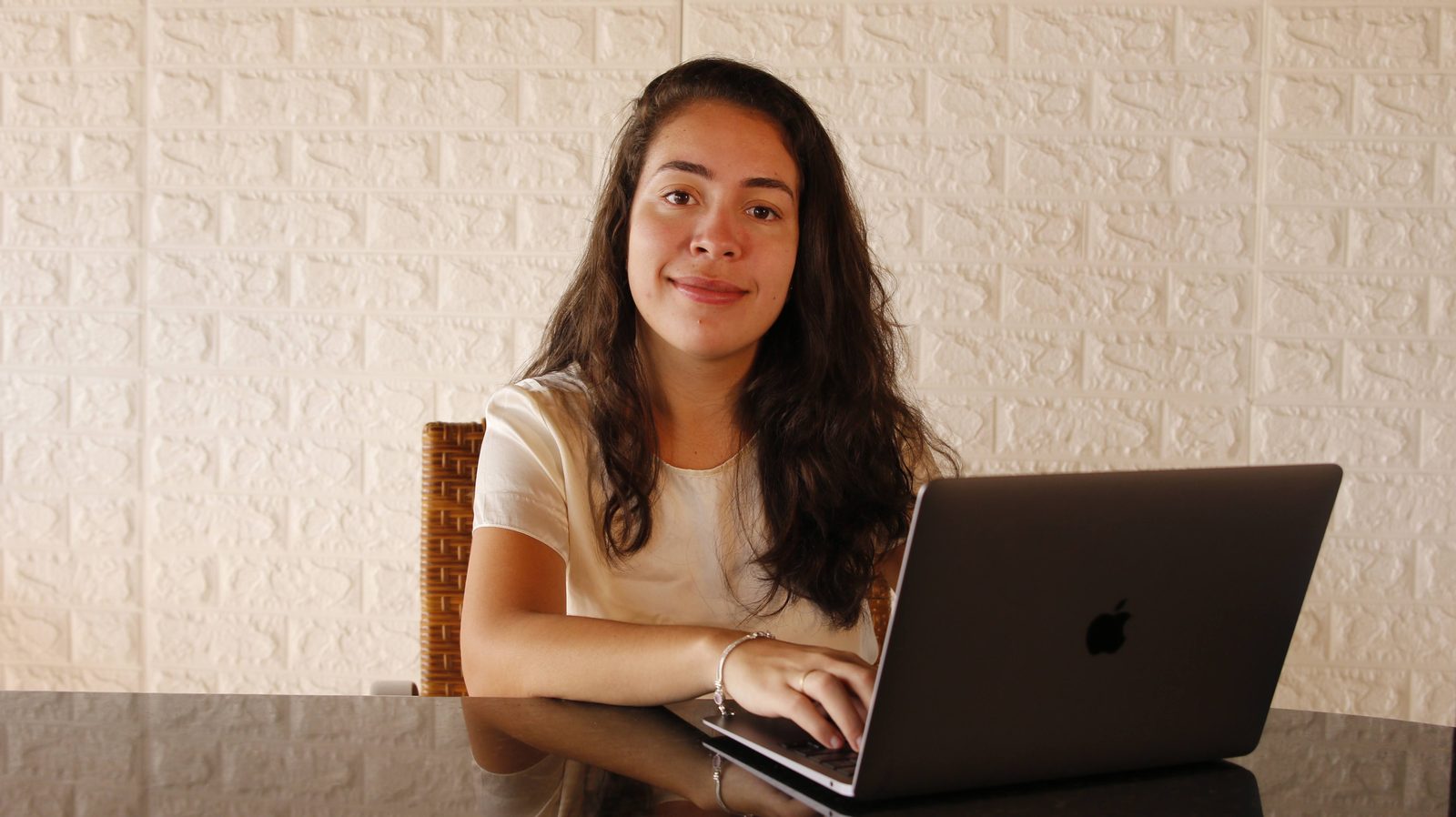 Karina Romano sentada à mesa de trabalho com o notebook aberto